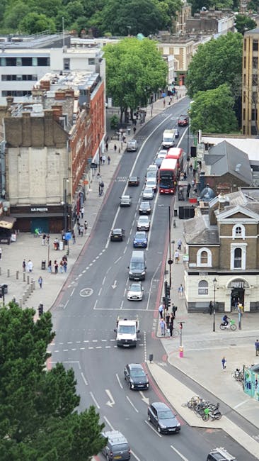 A busy street scene in South Harrow featuring a crosswalk with a green pedestrian signal, where several pedestrians are walking across the road. To the right, there is a multi-storey corner building w